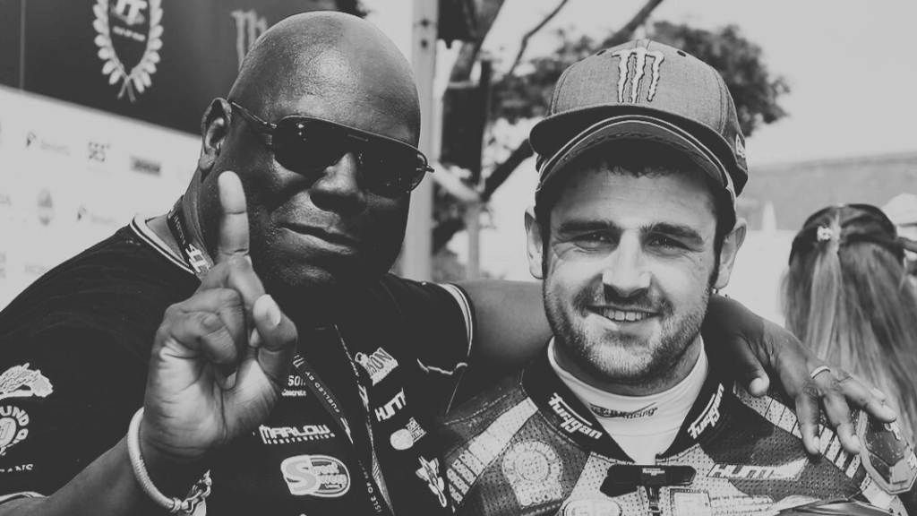 DJ Carl cox and Micheal Dunlop MBE posing together, one holding a helmet with visible branding.